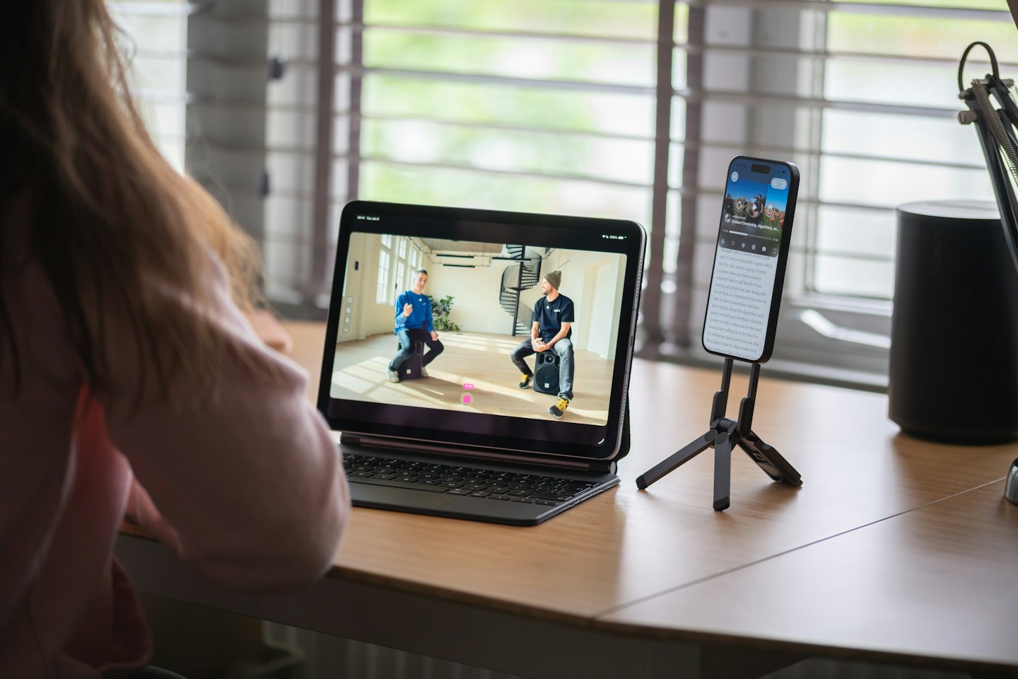 Person uses tablet and smartphone on a wooden desk.